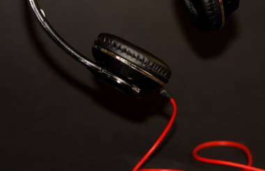 Siyah arka planda, kırmızı elementler ve kordon ile müzik dinlemek için büyük kulaklıklar. 