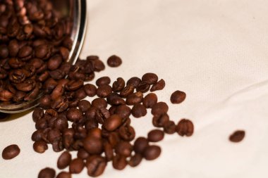Beyaz kaba kumaşın üzerinde depolamak için metal bir teneke kutudan taze Arabika kahvesi taneleri var..