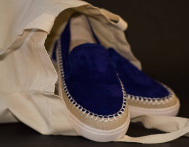 Alışveriş çantasının, alışverişçinin, bej kumaşın ve mavi süet terliklerin siyah arka planında. Sokak modası, kadın tarzı ayakkabılar..