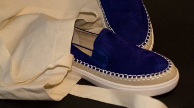 Alışveriş çantasının, alışverişçinin, bej kumaşın ve mavi süet terliklerin siyah arka planında. Sokak modası, kadın tarzı ayakkabılar..