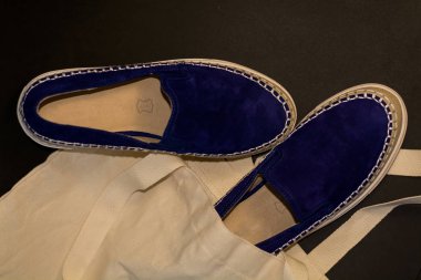 Alışveriş çantasının, alışverişçinin, bej kumaşın ve mavi süet terliklerin siyah arka planında. Sokak modası, kadın tarzı ayakkabılar..