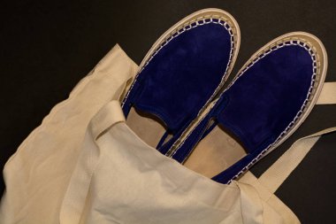 Alışveriş çantasının, alışverişçinin, bej kumaşın ve mavi süet terliklerin siyah arka planında. Sokak modası, kadın tarzı ayakkabılar..