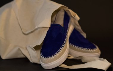 Alışveriş çantasının, alışverişçinin, bej kumaşın ve mavi süet terliklerin siyah arka planında. Sokak modası, kadın tarzı ayakkabılar..