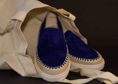 Alışveriş çantasının, alışverişçinin, bej kumaşın ve mavi süet terliklerin siyah arka planında. Sokak modası, kadın tarzı ayakkabılar..