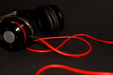 Siyah arka planda, kırmızı elementler ve kordon ile müzik dinlemek için büyük kulaklıklar. 