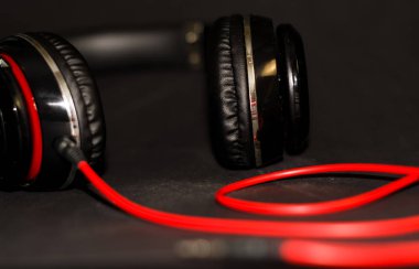 Siyah arka planda, kırmızı elementler ve kordon ile müzik dinlemek için büyük kulaklıklar. 