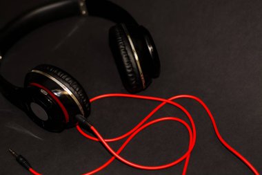 Siyah arka planda, kırmızı elementler ve kordon ile müzik dinlemek için büyük kulaklıklar. 