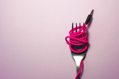 Pembe arka plan. Kırmızı, pembe, sarı kulaklık kablosu gümüş çatalla sarılı. Spagetti..