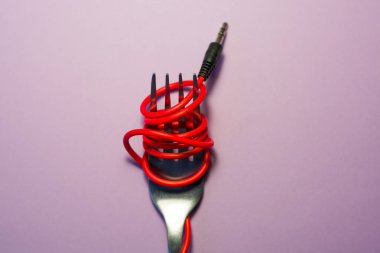 Pembe arka plan. Kırmızı, pembe, sarı kulaklık kablosu gümüş çatalla sarılı. Spagetti..