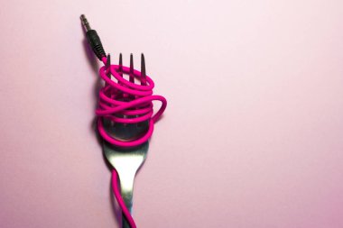 Pembe arka plan. Kırmızı, pembe, sarı kulaklık kablosu gümüş çatalla sarılı. Spagetti..