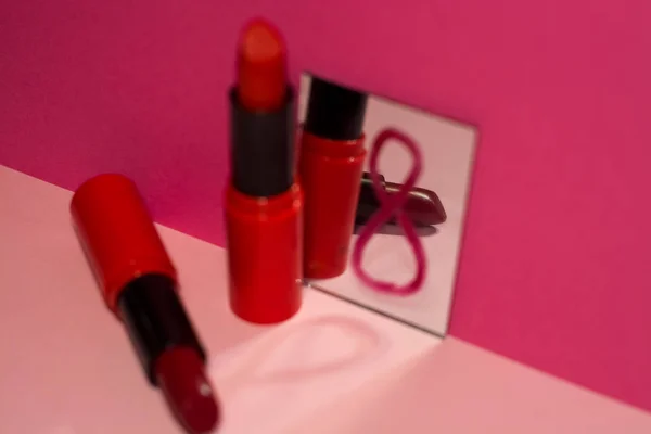 Red lipsticks and small mirror on bright pink background. Holiday is March eighth, day of women and spring.