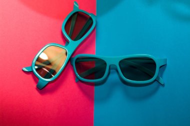 Parlak pembe arka planda siyah gözlüklü plastik mavi çerçeveli güneş gözlükleri uzanıyor. Yaz. Aksesuarlar.