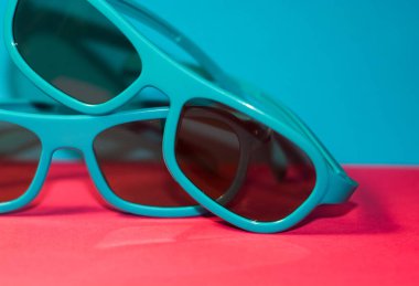 Parlak pembe arka planda siyah gözlüklü plastik mavi çerçeveli güneş gözlükleri uzanıyor. Yaz. Aksesuarlar.