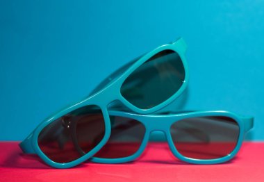 Parlak pembe arka planda siyah gözlüklü plastik mavi çerçeveli güneş gözlükleri uzanıyor. Yaz. Aksesuarlar.