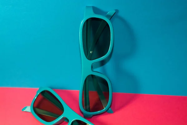 亮粉色背景的太阳镜是塑料蓝色相框和墨镜 — 图库照片