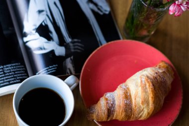 Kahve dükkanında kahvaltı. Bir fincan kahve ve taze kruvasan. Cam içinde çiçekler..