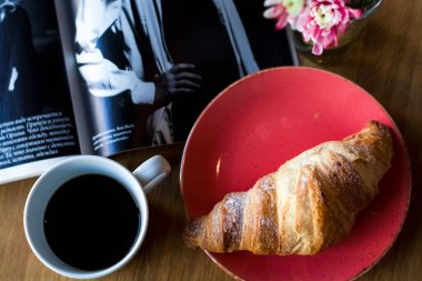 Kahve dükkanında kahvaltı. Bir fincan kahve ve taze kruvasan. Cam içinde çiçekler..