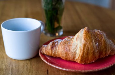 Kahve dükkanında kahvaltı. Bir fincan kahve ve taze kruvasan. Cam içinde çiçekler..