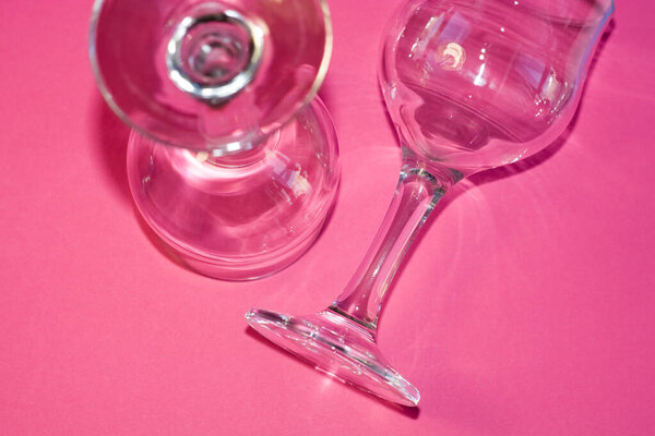 Glass transparent wine glasses on leg on pink background. Highlights and shadows on the dishes.