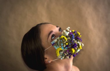 Renkli maskeli genç bayan tarla çiçeklerinin korumasıyla karşı karşıya. Modern moda ve tarz. Hava kirliliği veya virüs koronavirüsü salgını. 