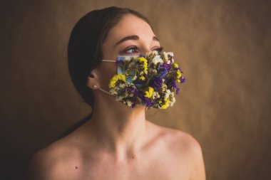 Renkli maskeli genç bayan tarla çiçeklerinin korumasıyla karşı karşıya. Modern moda ve tarz. Hava kirliliği veya virüs koronavirüsü salgını. 