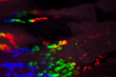 Dolu, çok renkli, gökkuşağı bokeh ve röfleli koyu soyut arkaplan.