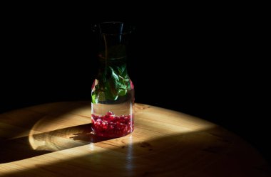 Siyah arka plan ve cam, nane ve nar taneleriyle su içmek, güneş ışınlarının karşısında durmak. Kullanışlı su.