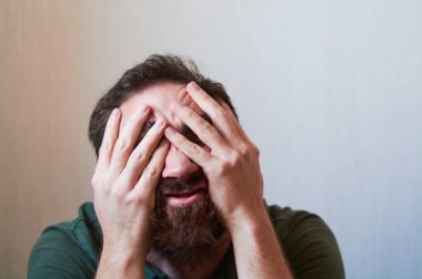 Siyah sakallı, yüzünde çeşitli duygular olan yeşil gömlekli genç bir adam portresi..