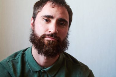 Siyah sakallı, yüzünde çeşitli duygular olan yeşil gömlekli genç bir adam portresi..