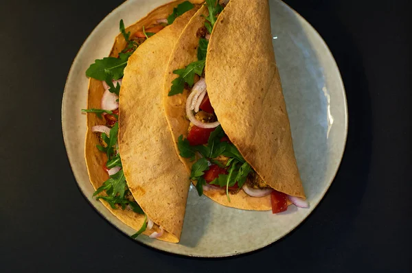 Plate with Mexican cuisine, large tacos with vegetables and meat on black background.