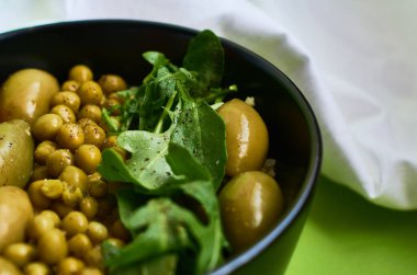 Yeşil yaz arkaplanı, siyah kâseli beyaz bez ve lezzetli bir kahvaltılık yulaf lapası ve sebze. Domates, zeytin, roka, bezelye.