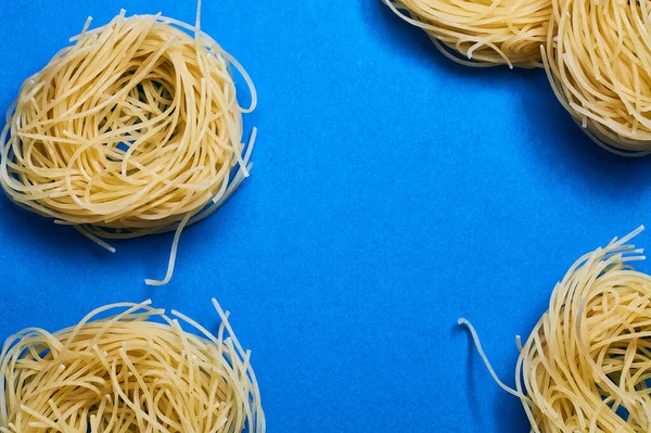 Blue background and Italian noodles, spaghetti, pasta of different forms of wheat in raw.