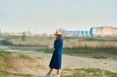 Mavi ceketli, bej şapkalı mutlu genç bayan baharın başında tarlada koşuyor..