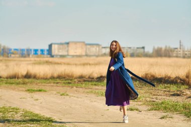 Mavi ceketli, bej şapkalı mutlu genç bayan baharın başında tarlada koşuyor..