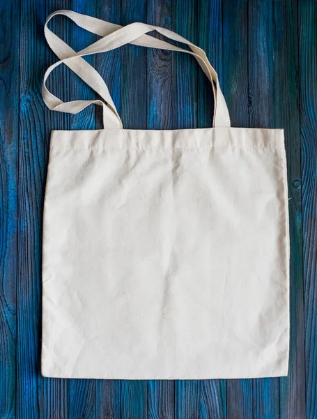 Fabric white shopper bag is empty for food purchases on blue wooden background.