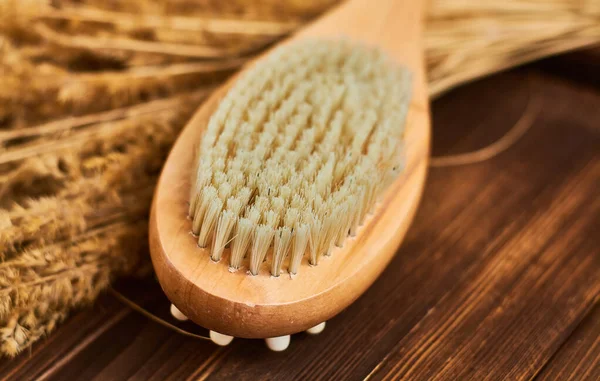 Wooden brush massage counter, washcloth for shower with double body nozzles with bunch of dried straw on dark background with place for inscription.