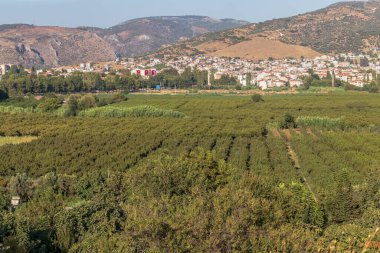 Bir tarım arazisinden yeşil ultra geniş bir manzara yayılıyor. Dağ ve çiftlik şehri var. Fotoğraf İzmir / Türkiye 'de çekildi.