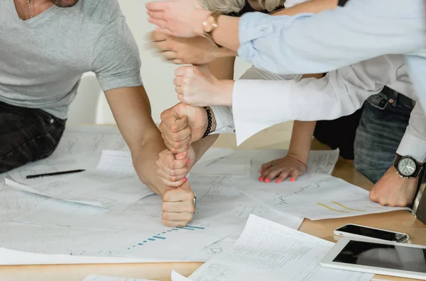 Corporate training employees build a pyramid of fists on the table On the table are pen drawings of tablets and telephones