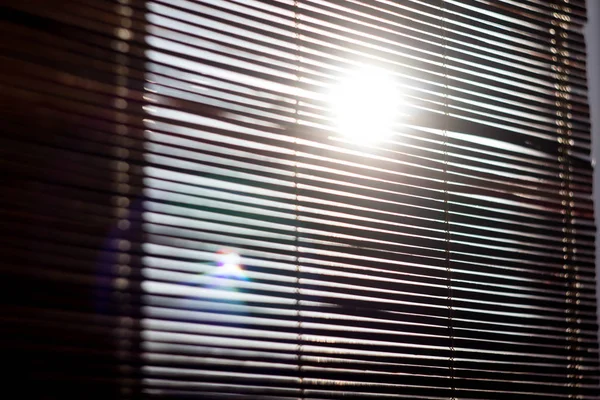 The sun shines through the wooden blinds on the window. The morning sun shines through the blinds consisting of wooden slats and planks.