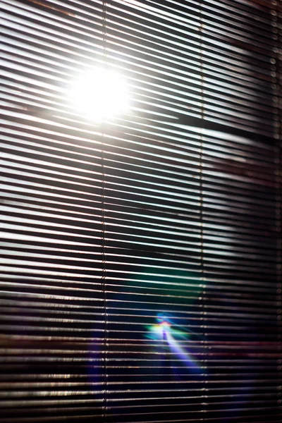 The sun shines through the wooden blinds on the window. The morning sun shines through the blinds consisting of wooden slats and planks.