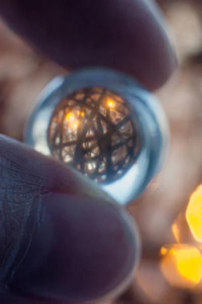 Reflection of a ball of twine in a glass ball. Fingers hold a glass ball through which shines a glowing ball and ropes