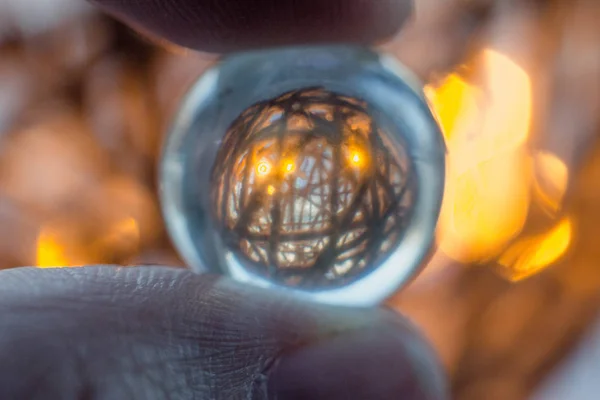 Reflection of a ball of twine in a glass ball. Fingers hold a glass ball through which shines a glowing ball and ropes