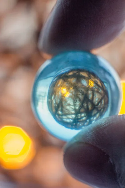 Reflection of a ball of twine in a glass ball. Fingers hold a glass ball through which shines a glowing ball and ropes