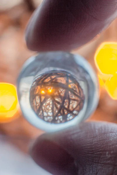 Reflection of a ball of twine in a glass ball. Fingers hold a glass ball through which shines a glowing ball and ropes