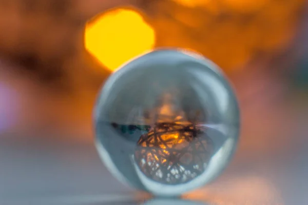 Reflection of a ball of twine in a glass ball. Fingers hold a glass ball through which shines a glowing ball and ropes