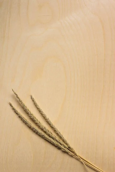 Three ears on a wooden background. Three ears of wheat lie on a wooden surface with yellow veins