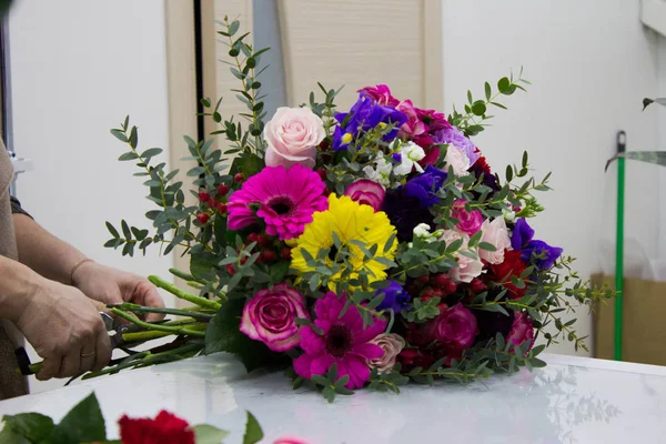 the hands of the florist make up a colorful bouquet of flowers on the table