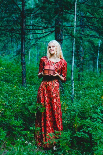blonde in a red dress in the woods with a chest in her hands