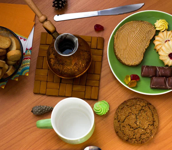 Coffee in a green mug and various sweets around on a wooden table. Peanut butter sandwich and candy cookie
