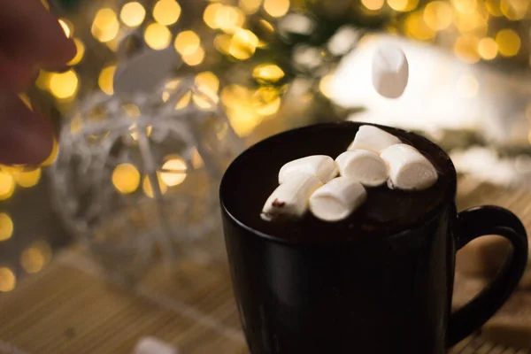 Strong coffee in a black mug. A white marshmallow drops into the mug from above.  The liquid splashes in different directions